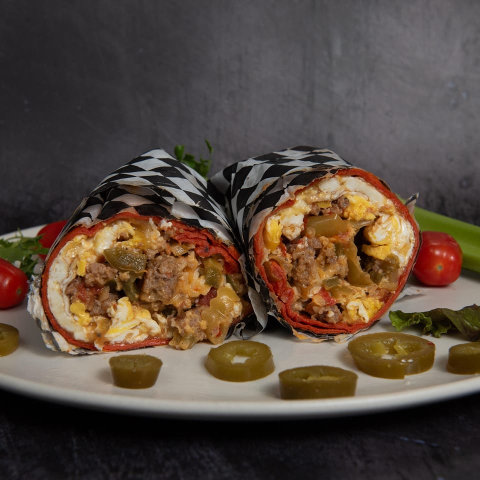 Two Mitchell's breakfast burritos, cut in half, revealing eggs, meat, and peppers, with jalapeños on a white plate.