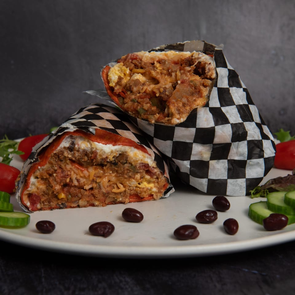 Two Mitchell's Breakfast Burritos, cut open to show fillings, on a plate with black beans and salad.