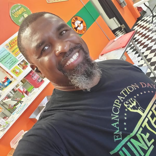 Smiling man with a gray beard wearing a black "Emancipation Day" shirt inside Mitchell's Breakfast Burritos.