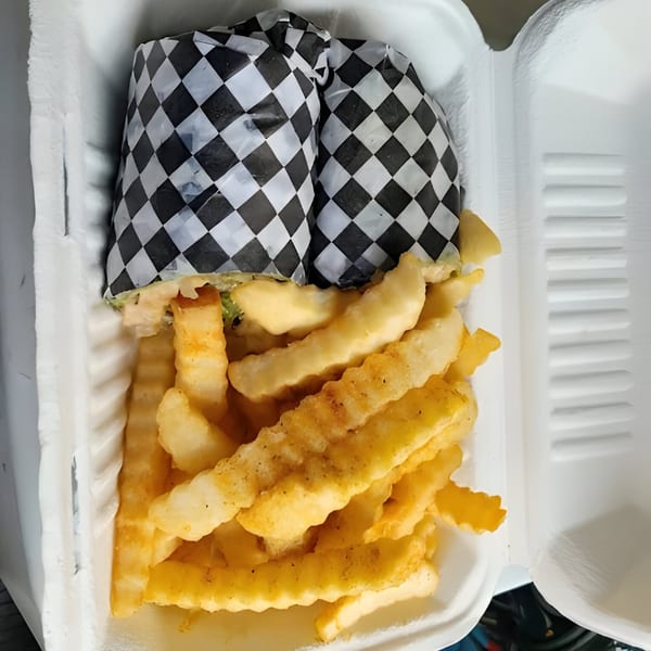 Two Mitchell's Breakfast Burritos wrapped in checkered paper, served with crinkle-cut fries in a to-go container.