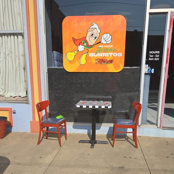 Mitchell's Breakfast Burritos storefront with a superhero burrito logo, two red chairs, and a checkerboard table.