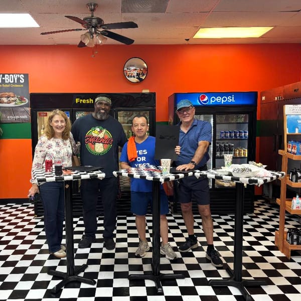 Four people stand around two checkerboard tables inside Mitchell's Breakfast Burritos, with orange walls and a checkered floor.