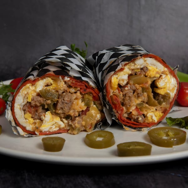 Two Mitchell's breakfast burritos, cut in half, revealing eggs, sausage, and peppers, with jalapeños.