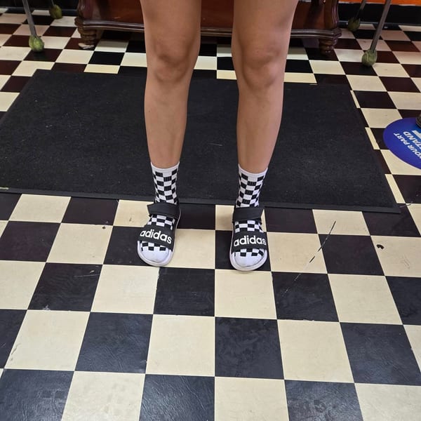 A person stands on a black and white checkered floor, wearing Adidas sandals and checkered socks.