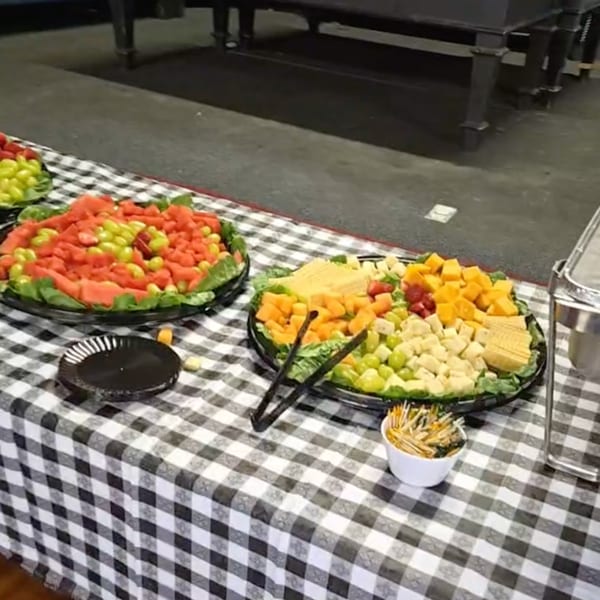 A buffet table with a black and white checkered tablecloth, featuring fruit and cheese platters.