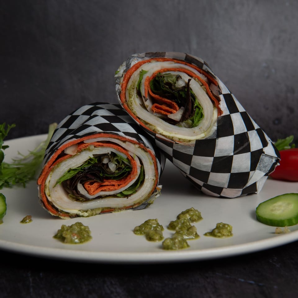 Two Mitchell's Breakfast Burritos, wrapped in checkered paper, filled with meat, lettuce, and orange tortilla.