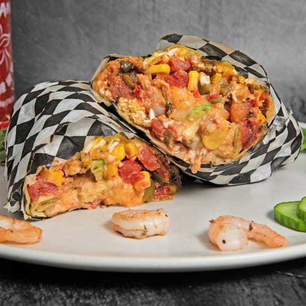 Two halves of a Mitchell's Breakfast Burrito, filled with eggs, corn, tomatoes, and cheese, on a white plate with shrimp.