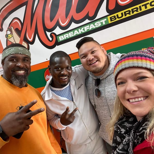 Four smiling people pose in front of a Mitchell's Breakfast Burritos sign.