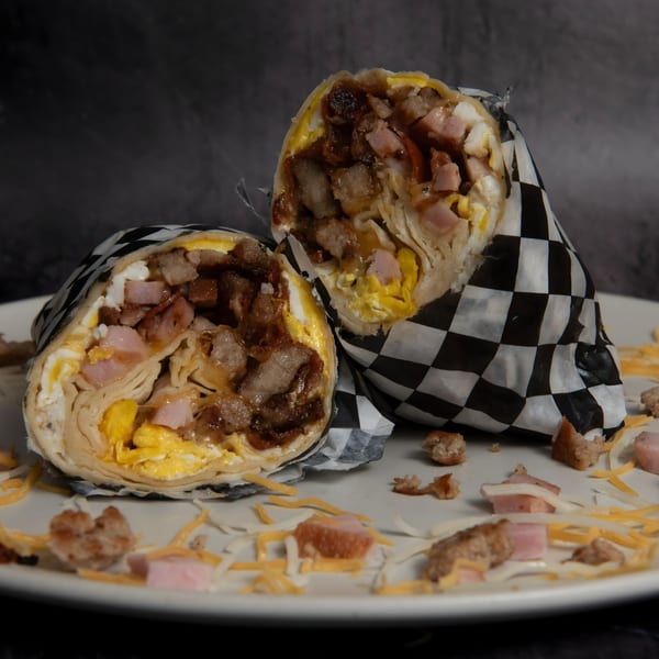 Two halves of a Mitchell's breakfast burrito, filled with eggs, ham, and sausage, on a white plate.