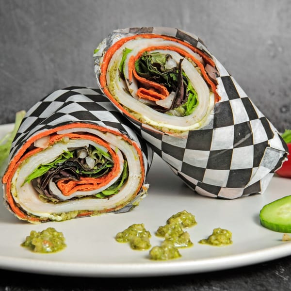 Two colorful Mitchell's burritos, wrapped in checkered paper, on a white plate with green sauce.