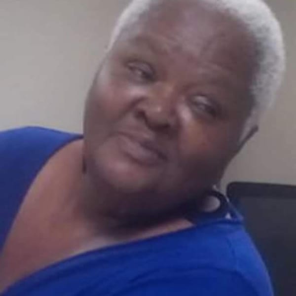 A woman with short white hair and a blue shirt looks to the side.