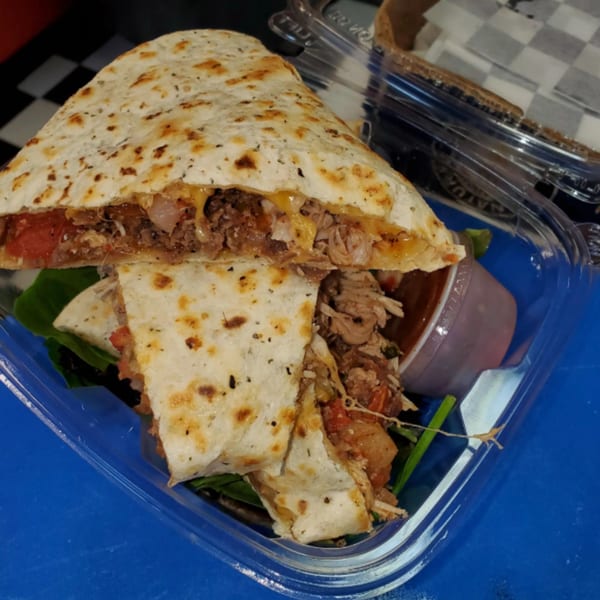 A large, cut quesadilla filled with meat, cheese, and vegetables, served with a side of salsa.